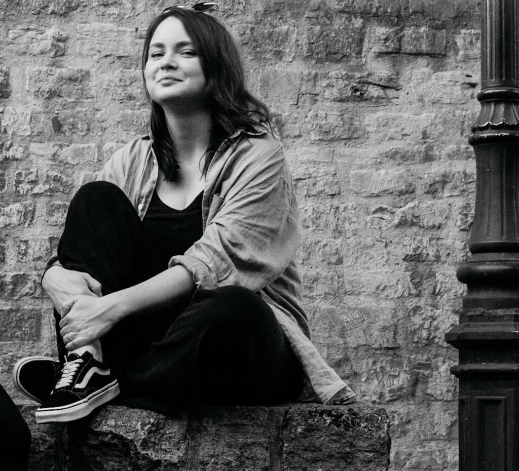 Tina sitzt auf einer Mauer und lächelt in die Kamera